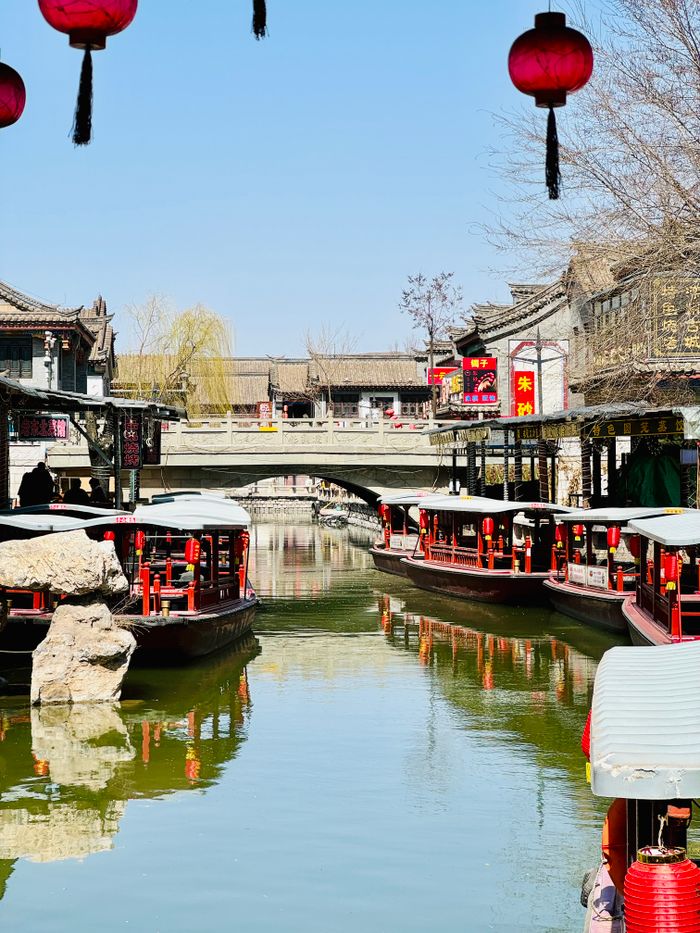 Traditional boats on a scenic canal in Tangshan, China, framed by rustic architecture and vibrant lanterns.